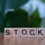 Close-up of wooden letter blocks spelling 'STOCK' on a table against a blurred green background.