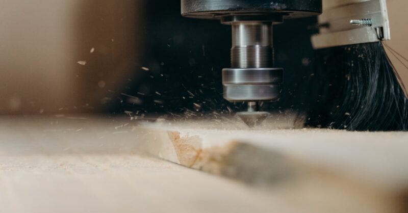 CNC machine in action, precisely cutting a wooden panel with sawdust flying.